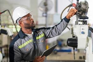engineer maintaining a robotic welding machine while holding a tablet computer