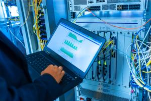 Technician with a laptop fixing network switch in data center room