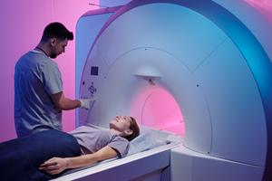 Young doctor pushing button on panel to start mri scan procedure while female patient lying on long table