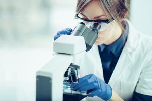 a scientist wearing personal protective equipment looks through a microscope in a laboratory